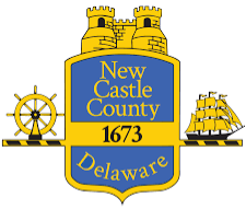 New Castle County, Delaware Logo of a blue crest featuring a yellow castle on top, a ship steering wheel on the left, and a ship on the right.
